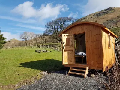 a wooden shed with a bed in a field at Stybeck Farm Shephards Hut in Thirlmere