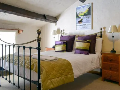 a bedroom with a bed with purple and yellow pillows at Rose Patch Cottage in Keswick