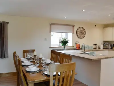 a dining room with a table with chairs and a kitchen at The Wheat Shed in Calthwaite
