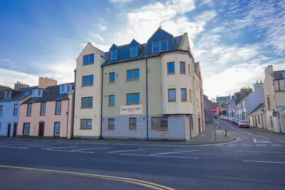 a large white building with blue windows on a street at Quay Head View Aparthotel in Stranraer