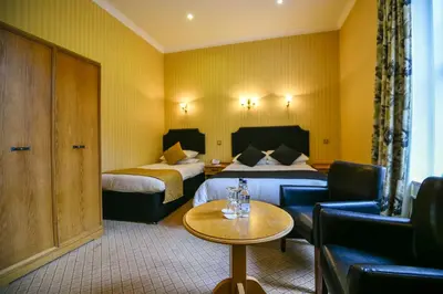 a hotel room with two beds and a table and a couch at Cairndale Hotel & Spa in Dumfries