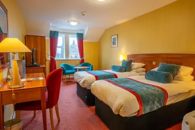 a hotel room with two beds and a desk at Cairndale Hotel & Spa in Dumfries