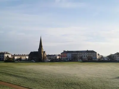 a large grass field with buildings and a church at The Golf Hotel in Silloth
