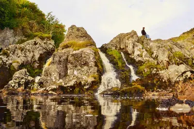 a man standing on a rock in front of a waterfall at Lagafater Lodge in Glenwhilly