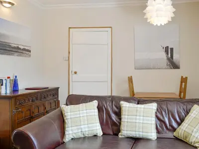 a brown leather couch in a living room with a chandelier at Mill Street in Drummore