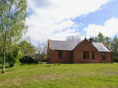 an old brick house on a green field at Perch Hall Cottage in Dinwoodie Mains
