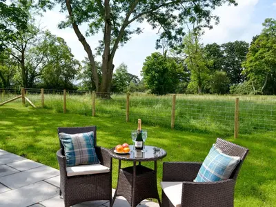 a patio with two chairs and a table with a bottle of wine at Bruno's Bothy in Wigton