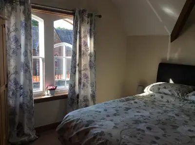 a bedroom with a bed and a window with curtains at St Matthews cottages in Allonby