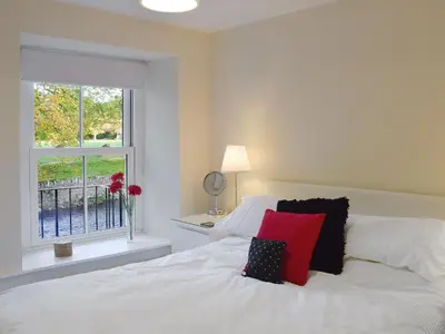 a white bed with a red pillow and a window at 1 Greta Side Court in Keswick