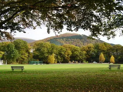two benches in a park with a mountain in the background at 2 Greta Side Court in Keswick