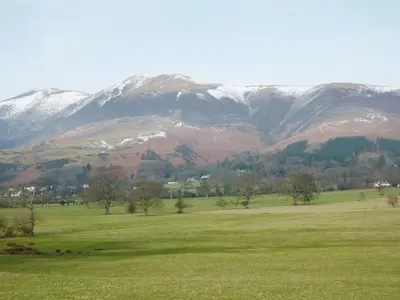 a field with snow covered mountains in the background at Acorn Lodge - Burnside Park in Keswick