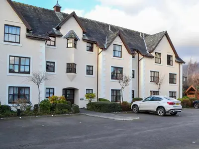 a white house with a car parked in a parking lot at Bleaberry- Hewetson Court in Keswick