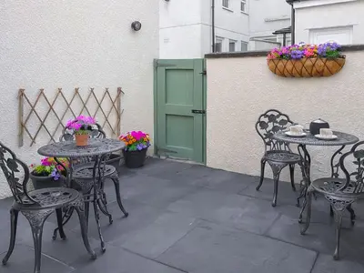 a patio with tables and chairs and a green door at Lavender Cottage in Keswick