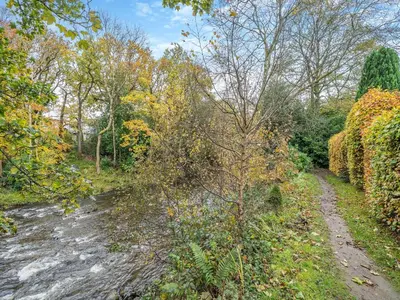 a dirt road next to a river with trees at Barleycorn in Keswick