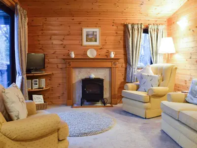 a living room with a fireplace and chairs and a tv at Fern Lodge- Burnside Park in Keswick