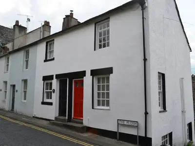 a white house with a red door on a street at 4 The Plosh in Keswick