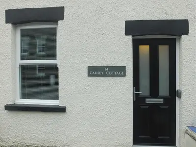 a white building with a black door and a window at Causey Cottage in Keswick