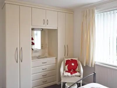 a bedroom with a dresser and a chair with a red pillow at Polperro in Keswick