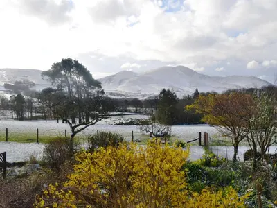 a snowy field with trees and mountains in the background at Overwater Lodge in Bassenthwaite Lake