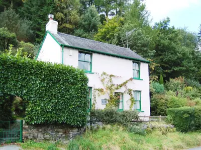 a white house with green windows and a hedge at Thwaite Hill Cottage in Braithwaite