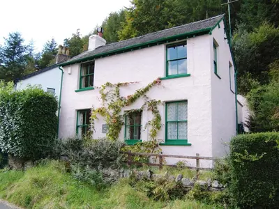 a white house with green windows on a hill at Thwaite Hill Cottage in Braithwaite