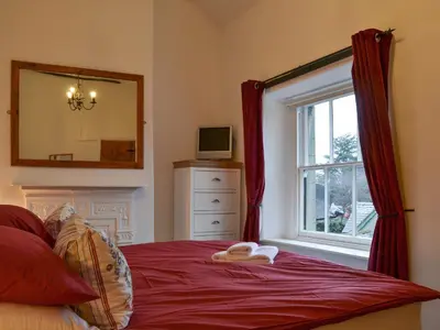 a bedroom with a bed with a mirror and a window at Croft Cottage in Braithwaite