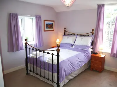 a bedroom with a bed with purple sheets and windows at Beech End in Braithwaite