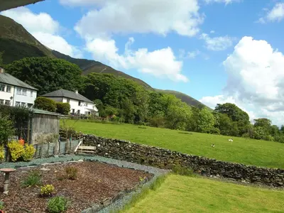 a garden with a stone wall and a field at Blease Cottage in Threlkeld