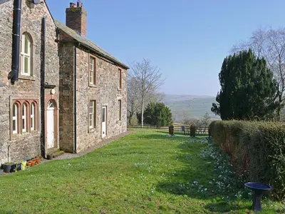 an old stone house with a grass yard in front of it at Laundry Cottage in Uldale