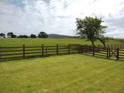 a wooden fence with a tree in the middle of a field at Greenrigg Cottage in Caldbeck
