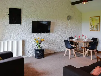 a living room with a table and a tv on a wall at Grooms Cottage in Plumbland