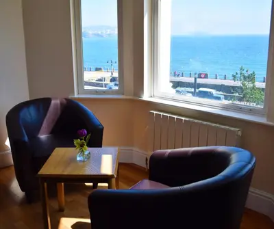 a living room with two chairs and a table and windows at The Sefton in Douglas