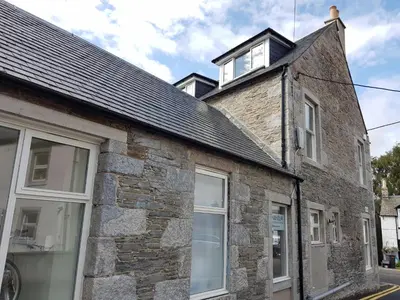 a stone house with a black roof and white windows at Barholm Accommodation in Creetown