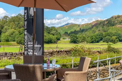 a table and chairs with an umbrella and mountains at The Lodge In The Vale in Thirlmere