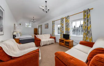 a living room with orange furniture and a bedroom at Muncaster Castle Coachman's Quarters in Ravenglass