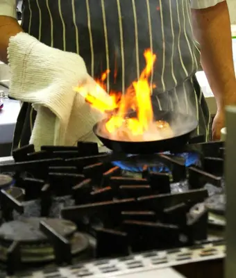 a man cooking food in a pan on a stove at Selkirk Arms Hotel in Kirkcudbright