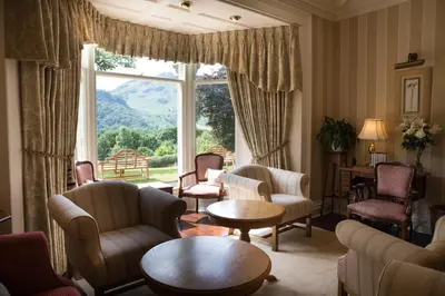 a living room with chairs and tables and a large window at Hazel Bank Country House Borrowdale Valley in Rosthwaite