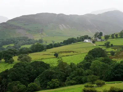 a green hillside with a house in the middle at YHA Eskdale in Eskdale