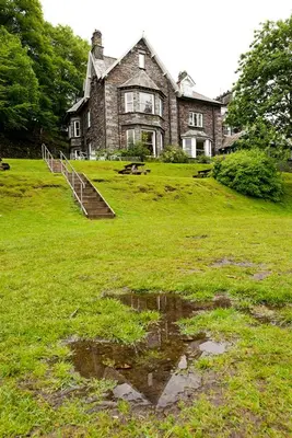 a house on a field with a puddle in the grass at YHA Grasmere Butharlyp Howe in Grasmere