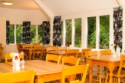 a restaurant with wooden tables and chairs and windows at YHA Grasmere Butharlyp Howe in Grasmere