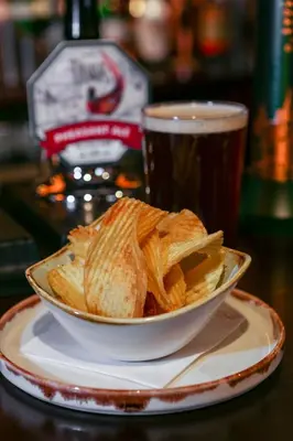 a bowl of chips on a plate next to a cup of beer at The Pheasant Inn - The Inn Collection Group in Bassenthwaite