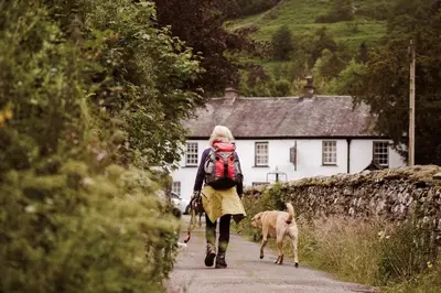 a woman walking a dog down a road at Royal Oak Hotel in Rosthwaite