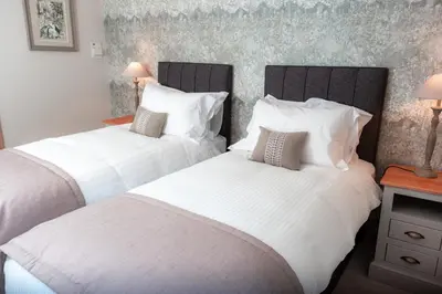 two beds in a bedroom with white sheets and pillows at The Ruddings in Keswick