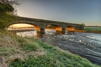 a stone bridge over a river with a sunset at Red Rose Cottage in Cockermouth