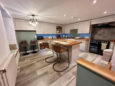 a kitchen with white cabinets and a island with chairs at Bakers Cottage in Cockermouth