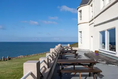 a row of picnic tables next to a building with the ocean at The Portpatrick Hotel by Compass Hospitality in Portpatrick