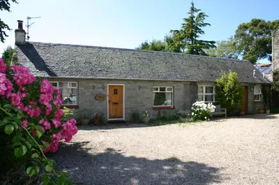 an old stone cottage with pink flowers in front of it at Woodcroft Cottage in Ayr