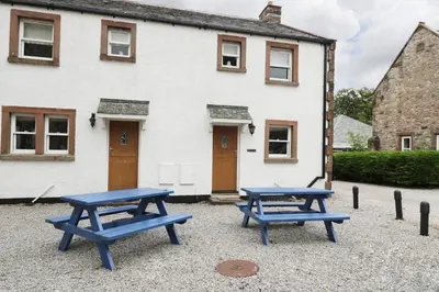 two blue picnic tables in front of a white house at William Court Cottage in Santon Bridge