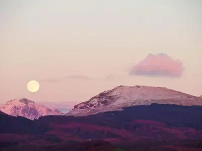 a moon rising over a mountain range with mountains at Gable View in Drigg