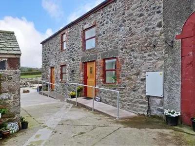 a stone building with orange doors and a gate outside at Gable View in Drigg